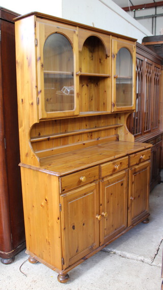A pine dresser the raised back with moulded cornice fitted a recess flanked by a pair of cupboards, the base fitted 3 long drawers above triple cupboards, raised on bun feet 191cm h x 131cm w x 44cm d 