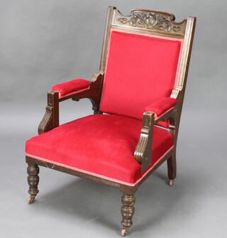 An Edwardian carved oak show frame open armchair, the seat and back upholstered in red material, raised on turned supports 