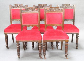 A set of five Edwardian carved oak dining chairs, the seats and backs upholstered in red material, raised on turned supports
