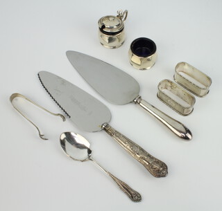 A pair of silver napkin rings Birmingham 1941, a pair of tongs, two cake slices, spoon and condiments 154 grams