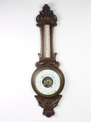 An Edwardian aneroid barometer and thermometer with paper dial contained in a carved oak wheel case 