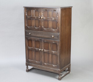 Ercol, a dark elm cocktail cabinet the upper section enclosed by a panelled door, the base fitted a drawer above double cupboard, raised on turned and block supports 127cm h x 82cm w x 43cm d 