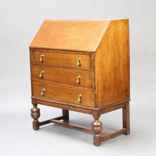 A 1930's oak bureau with fall front above 3 drawers, raised on cup and cover supports 95cm h x 75cm w x 43cm d 