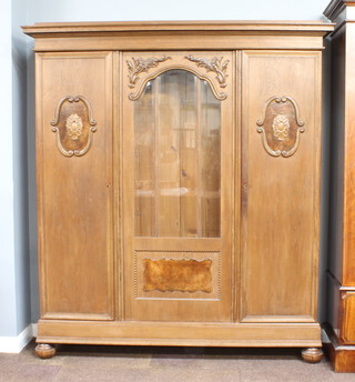 An Edwardian Dutch carved oak wardrobe, fitted shelves, the centre section enclosed by arched bevelled plate panelled door flanked by carved panelled doors and raised on bun feet 192cm h x 173cm w x 46cm d  