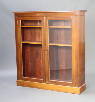 An Edwardian walnut bookcase, fitted shelves enclosed by glazed panelled doors, raised on a platform base 125cm h x 117cm w x 30cm d 