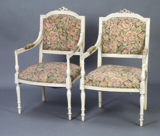 A pair of French Empire style white painted open arm salon chairs with upholstered seats and backs, raised on turned supports 