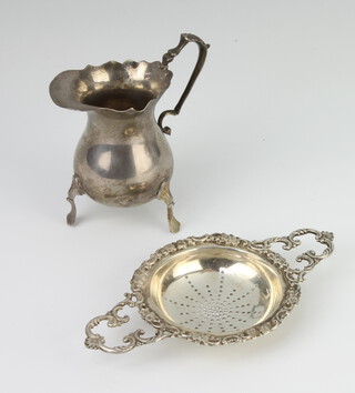 A silver 2 handled tea strainer with cast scroll rim, London 1960 together with a cream jug 202 grams 