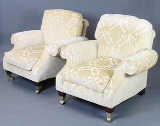 A pair of Georgian style armchairs upholstered in yellow sculpted material, raised on square tapered supports, brass caps and casters 