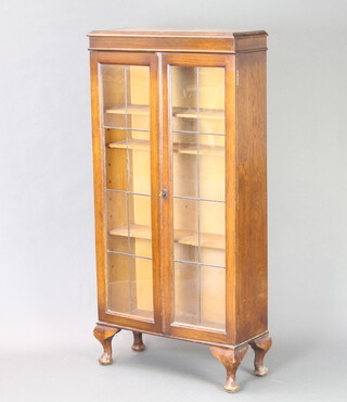 A 1930's oak bookcase fitted adjustable shelves enclosed by lead glazed panelled doors 123cm h x 60cm w x 23cm d, raised on cabriole supports (1 glass panel missing) 