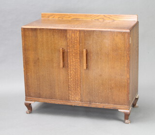 A 1930's Art Deco oak cabinet with raised back and fitted interior enclosed by panelled doors, raised on cabriole supports 90cm h x 99cm w x 46cm d 
