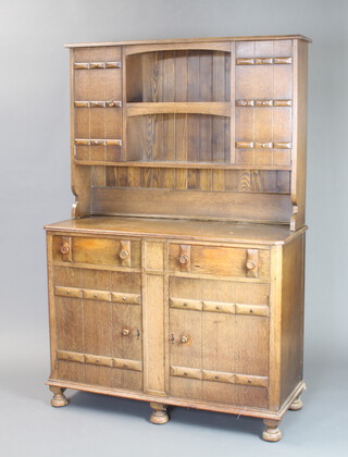 An oak dresser, the raised back fitted a shelf and cupboards enclosed by panelled doors above a recess, the base fitted 2 drawers and double cupboard, raised on bun feet 180cm h x 121cm w x 48cm d 