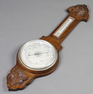 An aneroid barometer and thermometer with silvered dial contained in a carved oak wheel case, (section of timber missing to the top of the thermometer)