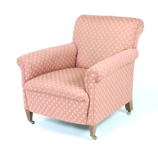 An Edwardian Howard style armchair upholstered in pink and gold material, raised on square inlaid mahogany supports with brass caps and casters 