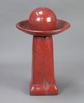 A red glazed circular garden globe water feature within a dish raised on a pedestal column 70cm h x 40cm diam. (a crack to the base)  