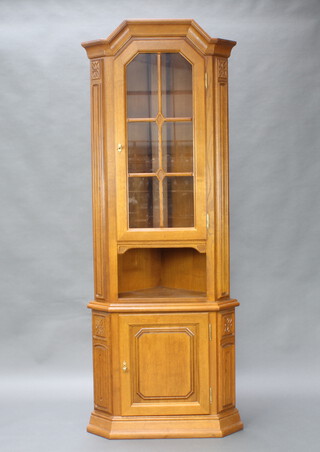 An American style light elm corner cabinet, the shelved interior enclosed by astragal glazed panelled doors above a enclosed by a panelled door 211cm h x 79cm w x 51cm d 