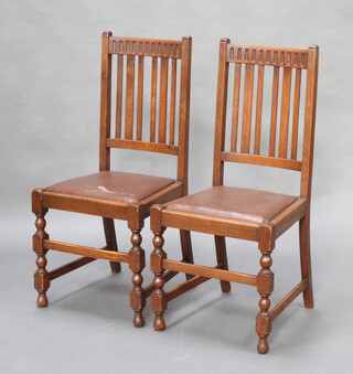 A pair of 1930's oak stick and rail back dining chairs with upholstered drop in seats, raised on turned and block supports 