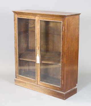A 1930's oak bookcase fitted adjustable shelves enclosed by glazed panelled doors, on a platform base 112cm h x 95cm w x 34cm d 

