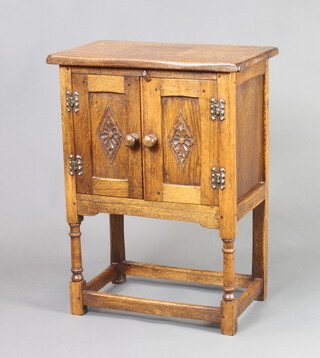 A carved oak cabinet enclosed by panelled doors, raised on turned supports with box stretcher 69cm h x 51cm w x 33cm d 
