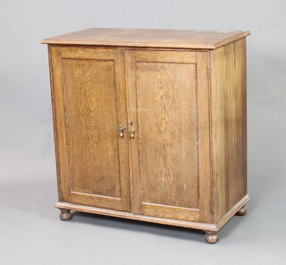 A 1930's bleached oak cabinet enclosed by a panelled door, raised on bun feet 83cm h x 80cm w x 42cm d  