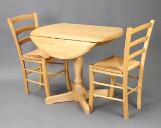A beech finished drop flap kitchen table raised on turned column and cruciform base 72cm h x 90cm w x 54cm d together with a pair of beech framed ladder back dining chairs 
