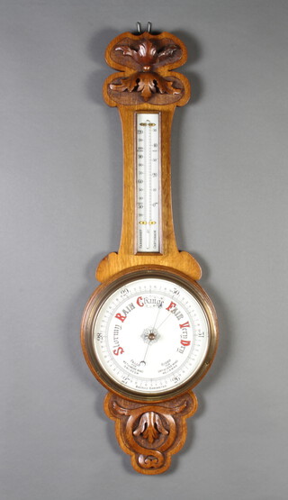 A late Victorian aneroid barometer and thermometer with porcelain dial, contained in a carved oak wheel case 