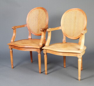A pair of Empire style bleached hardwood open arm chairs with woven cane seats and backs, raised on turned and fluted supports  