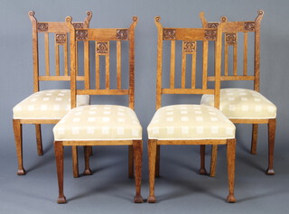 A set of 4 Art Nouveau Liberty style carved oak stick and rail back dining chairs with over stuffed seats, raised on square supports 