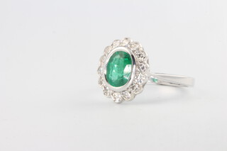 An 18ct white gold oval emerald and diamond cluster ring, the centre stone approx. 1.25ct, the 14 brilliant cut diamonds approx. 0.4ct, 4.3 grams, size N 