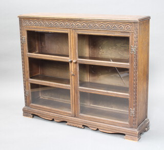 A carved oak display cabinet enclosed by glazed panelled doors on bracket feet 100cm h x 117cm w x 26cm d (light water marks to the top)