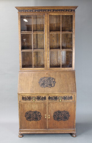 A 1930's carved oak bureau bookcase with moulded cornice, the upper section enclosed by astragal glazed panelled doors, the base with fall front above 2 drawers and double cupboard, on bun feet 209cm h x 98cm w x 54cm d  