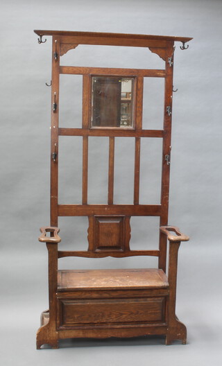 An Art Nouveau oak hall stand with bevelled plate mirror to the back, the base fitted a seat with hinged lid, complete with metal drip trays 192cm h x 99cm w x 38cm d (The silvering to the mirror shows sign of deterioration and there is some water damage to the seat) 