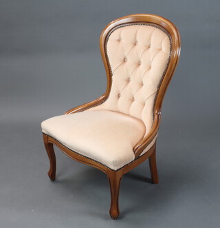 A Victorian style beech show frame nursing chair upholstered in peach coloured material raised on cabriole supports 