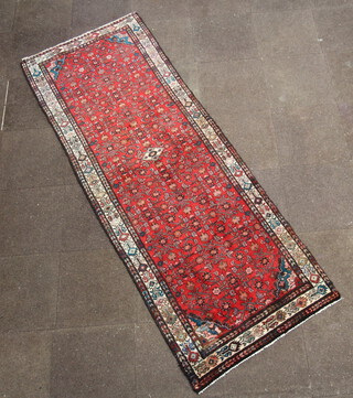 A red ground Persian rug with all over geometric design within a 3 row border 287cm x 104cm 