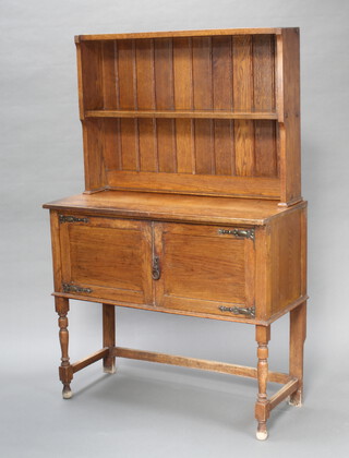 An Art Nouveau Liberty style oak dresser, the raised back fitted 2 shelves, the base enclosed by panelled doors, raised on turned and block supports 160cm h x 101cm w x 43cm d 