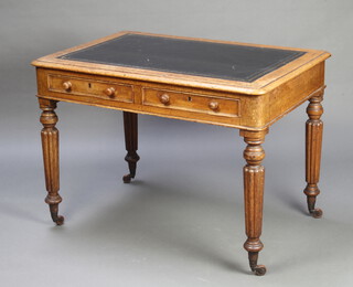 A Victorian Gillows style oak writing table with black inset leather writing surface, fitted 2 drawers, raised on turned and reeded supports, brass caps and castors 74cm h x 103cm w x 69cm d 