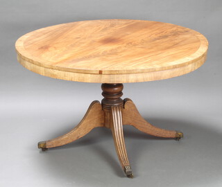 A Regency circular snap top bleached and crossbanded mahogany breakfast table, raised on a turned column and tripod supports ending in brass caps and castors 71cm h x 120cm diam. 