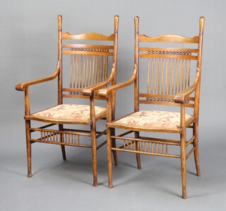 A pair of Edwardian Art Nouveau Liberty style oak stick and rail back carver chairs, the seats of serpentine outline raised on turned supports with box stretcher 104cm h x 56cm w x 46cm d (internal seat measurement 40cm w x 39cm d) 