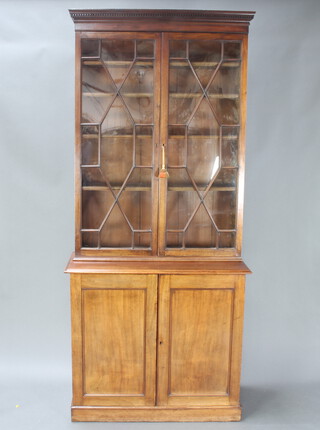 A Georgian mahogany bookcase on cabinet, the upper section with moulded and dentil cornice, fitted shelves enclosed by astragal glazed panelled doors, the base fitted 2 drawers above a shelved interior enclosed by panelled doors, raised on a platform base 235cm h x 104cm w x 49cm d 