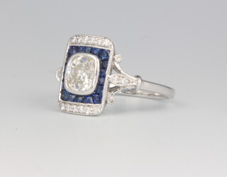 An 18ct white gold Art Deco style cocktail ring, the centre brilliant cut stone approx. 0.9ct surrounded by sapphires with diamonds to the scroll shoulders, size N, 3.3 grams 