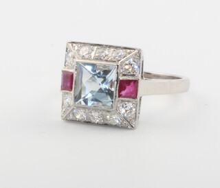 A platinum Art Deco style square aquamarine with diamond and ruby surround ring, the central stone approx. 1.30ct, the diamonds 0.60ct, size P