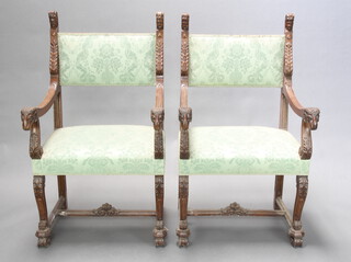 A pair of Italian style carved walnut open arm chairs with mask and rams head decoration, the seats and backs upholstered in sculpted green material, raised on shaped supports with H framed stretcher 109cm h x 63cm w x 57cm d (seat 48cm x 39cm) 