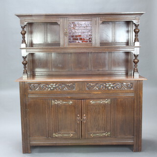 An Art Nouveau carved oak dresser, the raised back with moulded cornice fitted a cupboard enclosed by lead glazed panelled doors flanked by recesses, raised on cup and cover supports, the base fitted 2 drawers above double cupboard 169cm h x 152cm w x 53cm d 