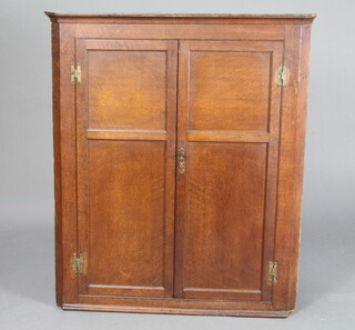 An 18th/19th Century oak corner cabinet with moulded cornice and barrel back, fitted shelves enclosed by panelled doors with H framed brass hinges 112cm h x 96cm w x 36cm d 