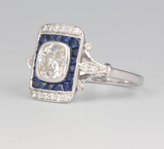 An 18ct white gold Art Deco style cocktail ring, the centre brilliant cut stone approx. 0.9ct surrounded by sapphires with diamonds to the scroll shoulders, size N, 3.3 grams 