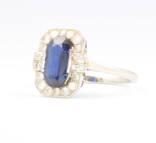 An Art Deco platinum, sapphire and diamond cocktail ring, the centre rectangular cut sapphire 10mm x 5mm surrounded by brilliant cut diamonds, size N