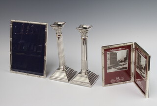 A Sterling silver easel photograph frame 25cm h x 19cm, a silver plated double photograph frame 18cm x 28cm and a pair of silver plated reeded candlesticks with Corinthian columns, raised on square bases 26cm x 10cm x 10cm  
