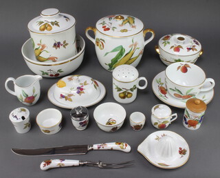 An extensive Royal Worcester Evesham tea, coffee, dinner and table service comprising a 3 piece carving set, knife, cake knife, scoop and pickle fork, lemon squeezer, oval casserole and lid, sauce boat and lid, 6 ramekins, teapot, 2 large ramekins, 2 pots and covers, 6 small storage jars, 2 large storage jars, cylindrical box and cover, 4 medium tea cups, 2 large tea cups, 6 coffee cups, 3 egg coddlers, lidded salt, 3 oil bottles, circular tureen and cover, deep tureen and cover, an oval dish, rectangular pie dish, butter dish and cover, 11 small plates, sauce kettle, milk jug, cream jug, tea infuser, 4 egg cups, an oval dish, soup tureen and cover, fruit bowl, hors d'oeuvres dish, storage jar and lid, giant tea cup and saucer, 5 small bowls, 2 dessert bowls, shell shaped dish, flour shaker, 2 souffle dishes, 6 lidded cups, 4 soup bowls, 1 deep bowl, 1 mug, pestle and mortar, cylindrical jar, deep bowl, salt and peppers, 2 shell butter dishes, an oval dish, 3 flan dishes, 5 small plates, 4 medium plates, 12 large dinner plates 