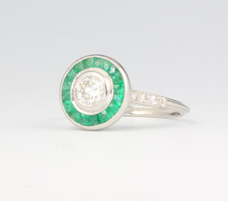 A platinum emerald and diamond Art Deco style ring, the centre brilliant cut diamond approx. 0.44ct surrounded by emeralds and diamond shoulders, 4.4 grams, size O