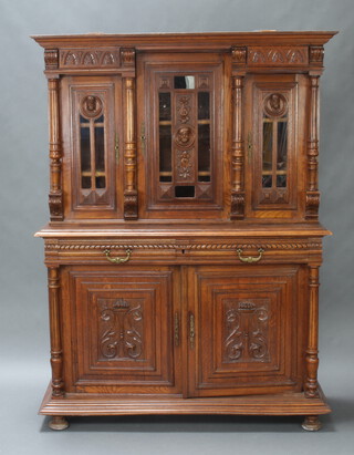 A 19th Century French carved oak dresser, the upper section with moulded cornice, fitted triple cupboards enclosed by glazed panelled doors with carved mast decoration, fluted columns to the side, base fitted 2 drawers above carved panelled doors 191cm h x 140cm w x 51cm d 