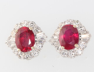 A pair of 18ct white gold oval ruby and diamond cluster earrings, the centre oval treated stones approx 5.4ct in total surrounded by brilliant and tapered baguette diamonds approx. 1.7ct, 14mm x 14mm, 6.8grams